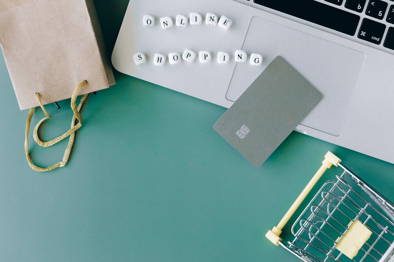 Flat lay of online shopping essentials with laptop, card, and shopping cart.