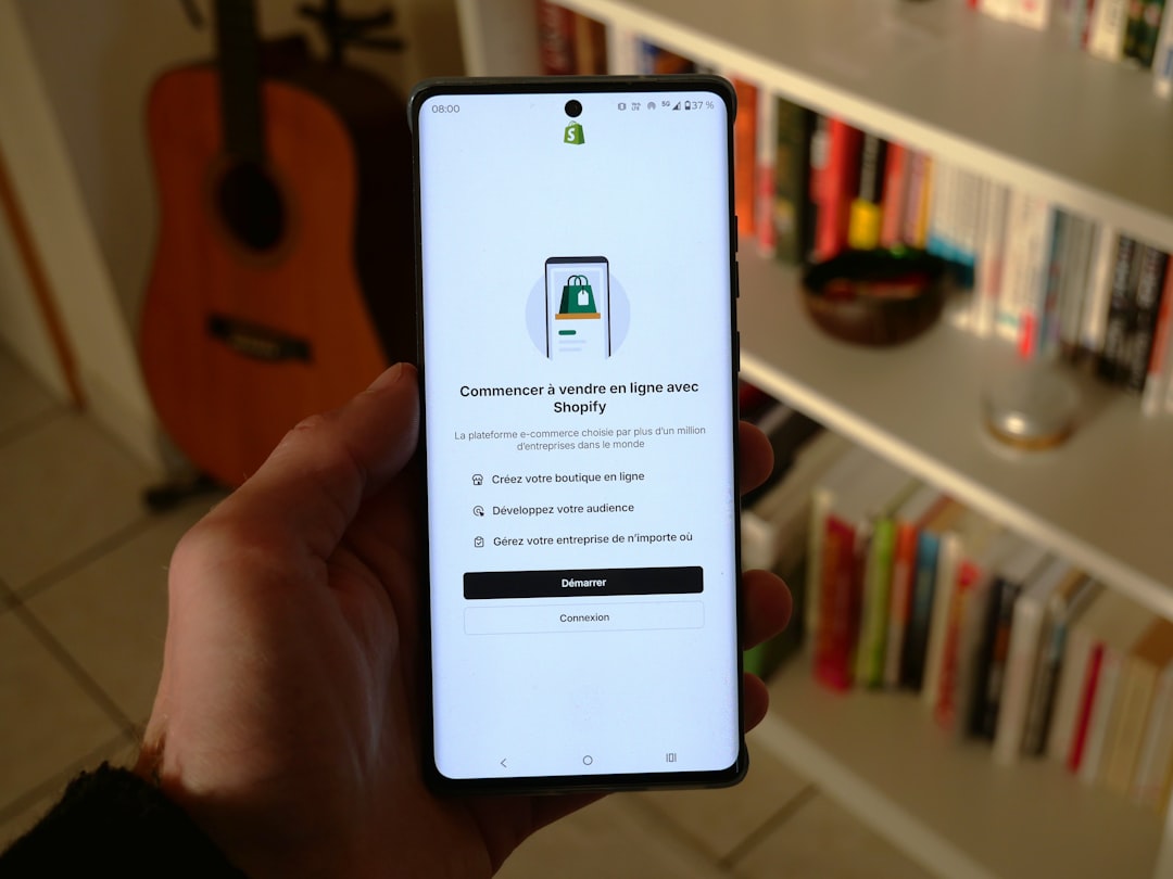 services-02 a hand holding a smartphone displaying the welcome screen of the Shopify app. The app interface is in French and invites users to start selling online with Shopify. It presents three options: Create your online store, Grow your audience, and Manage your business from anywhere. Two buttons are visible at the bottom of the screen: Start and Login.